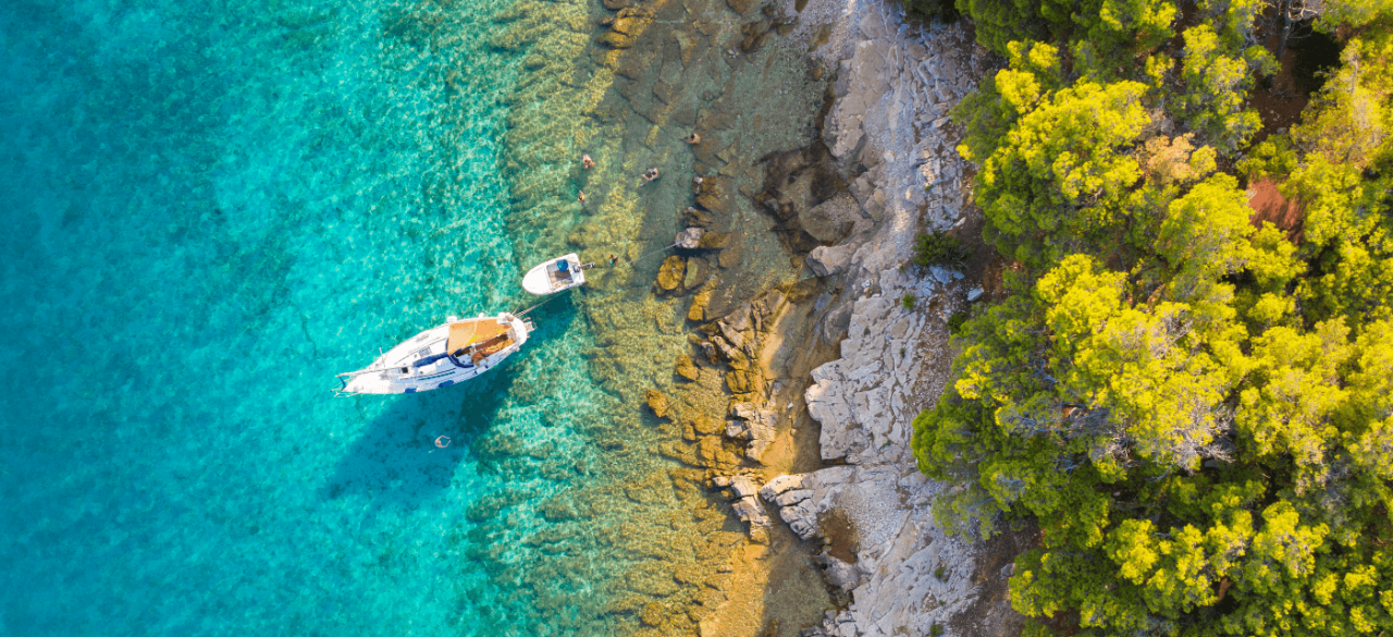 Yacht approaching rocks in azure ocean